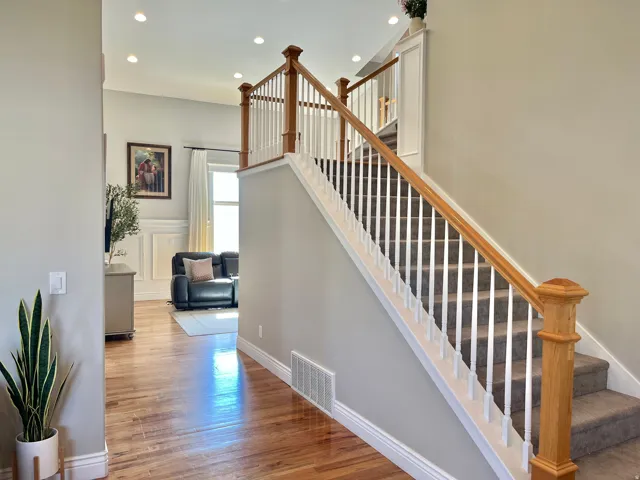 Inviting entryway featuring hardwood flooring, a carpeted staircase with wood and white balusters, recessed lighting, and white baseboards