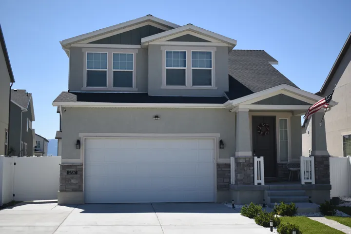 Contemporary two-story residence featuring a covered porch with stone accents, a two-car garage, and a crisp white perimeter fence