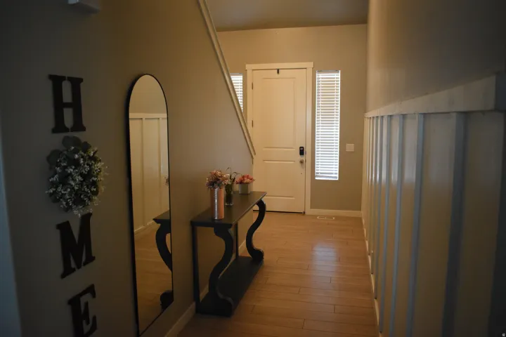 Entryway featuring wood-finish flooring, a contemporary front door with an adjacent vertical window, and wainscoting along the wall