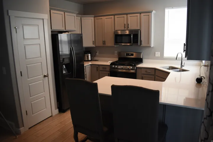 Contemporary kitchen featuring light gray cabinetry, stainless steel appliances, white countertops, and wood-finish flooring