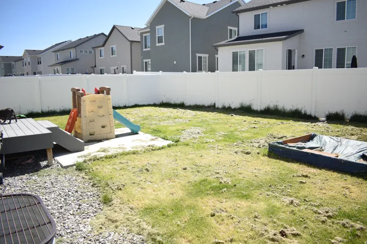 Expansive backyard featuring a white vinyl privacy fence, a concrete patio area, and a gravel section