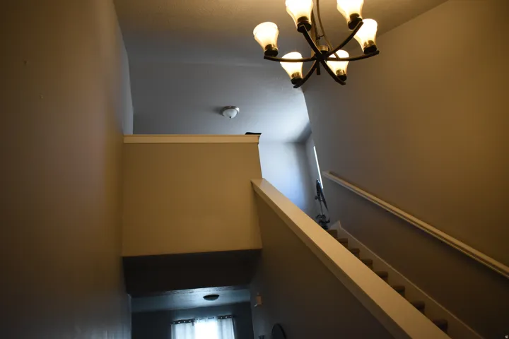 Staircase featuring a white handrail, neutral wall paint, and a multi-bulb chandelier