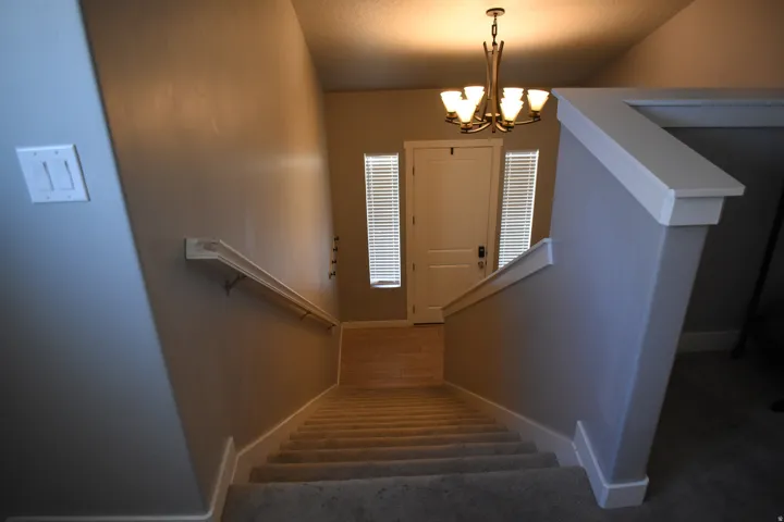 Staircase featuring carpeted treads, a painted handrail, and a chandelier lighting the entry