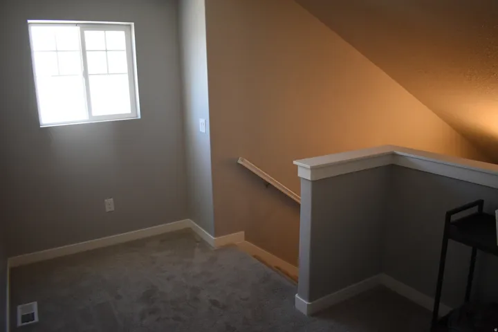Carpeted landing featuring a window with grid inserts, neutral wall color, white trim, and a partial balustrade
