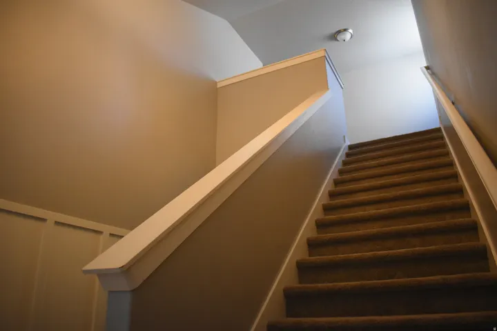 Carpeted staircase featuring a light beige wall color, white handrails, and a contemporary flush-mount ceiling light