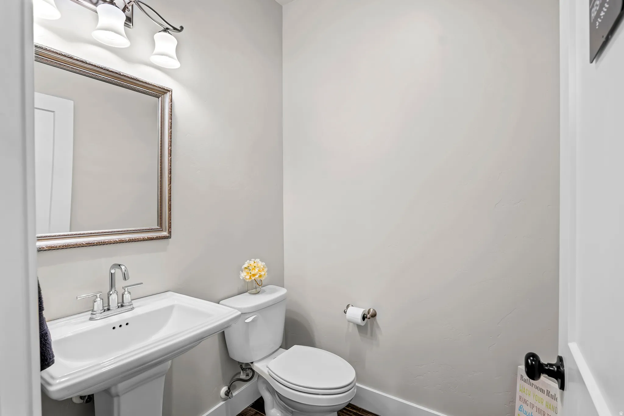 Pedestal sink with chrome faucet, framed mirror, and a three-light vanity fixture
