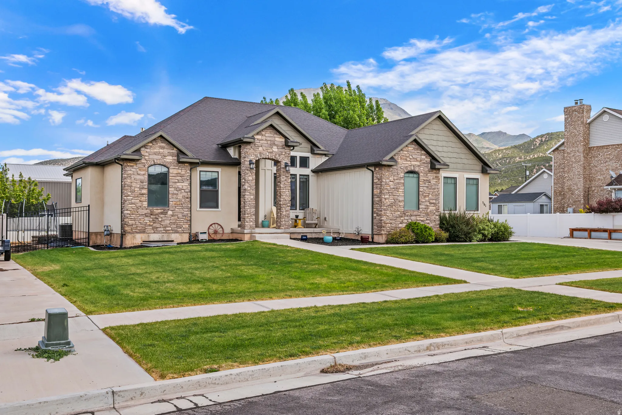 Stucco and stone facade home featuring a dark shingle roof, arched windows, and a manicured lawn