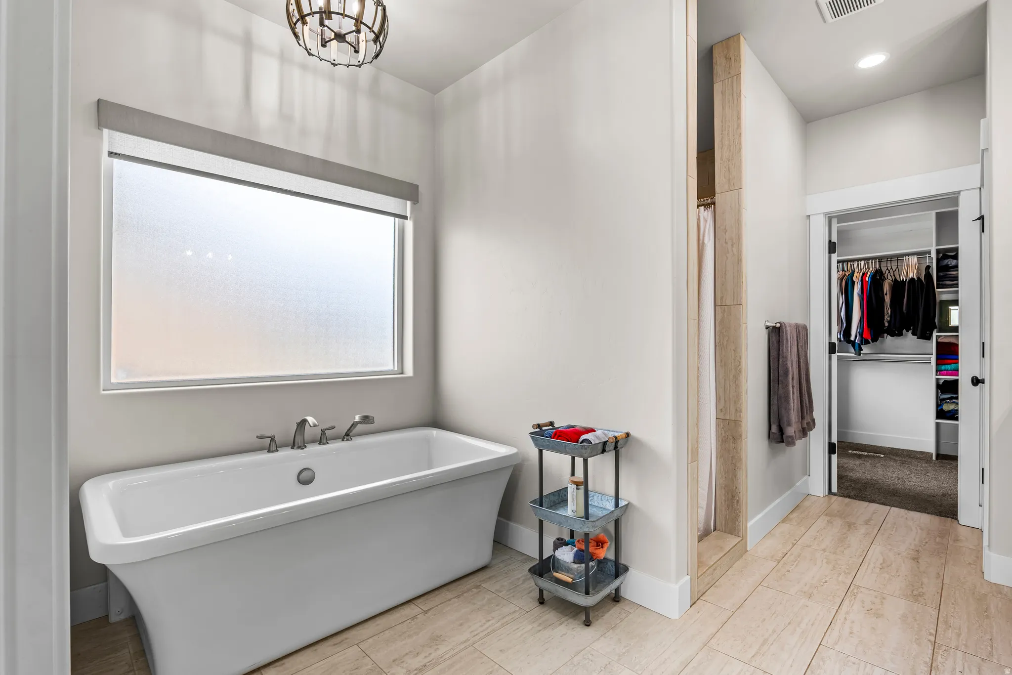 Freestanding soaking tub with brushed nickel fixtures below a large frosted window