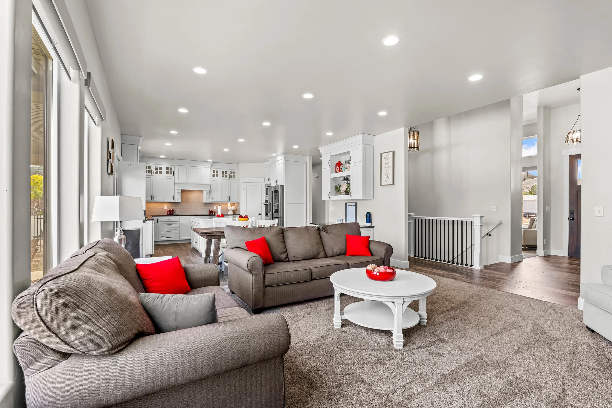 Open-concept living space featuring recessed lighting, large windows, light-toned walls, and a visible kitchen with white cabinetry and dark countertops