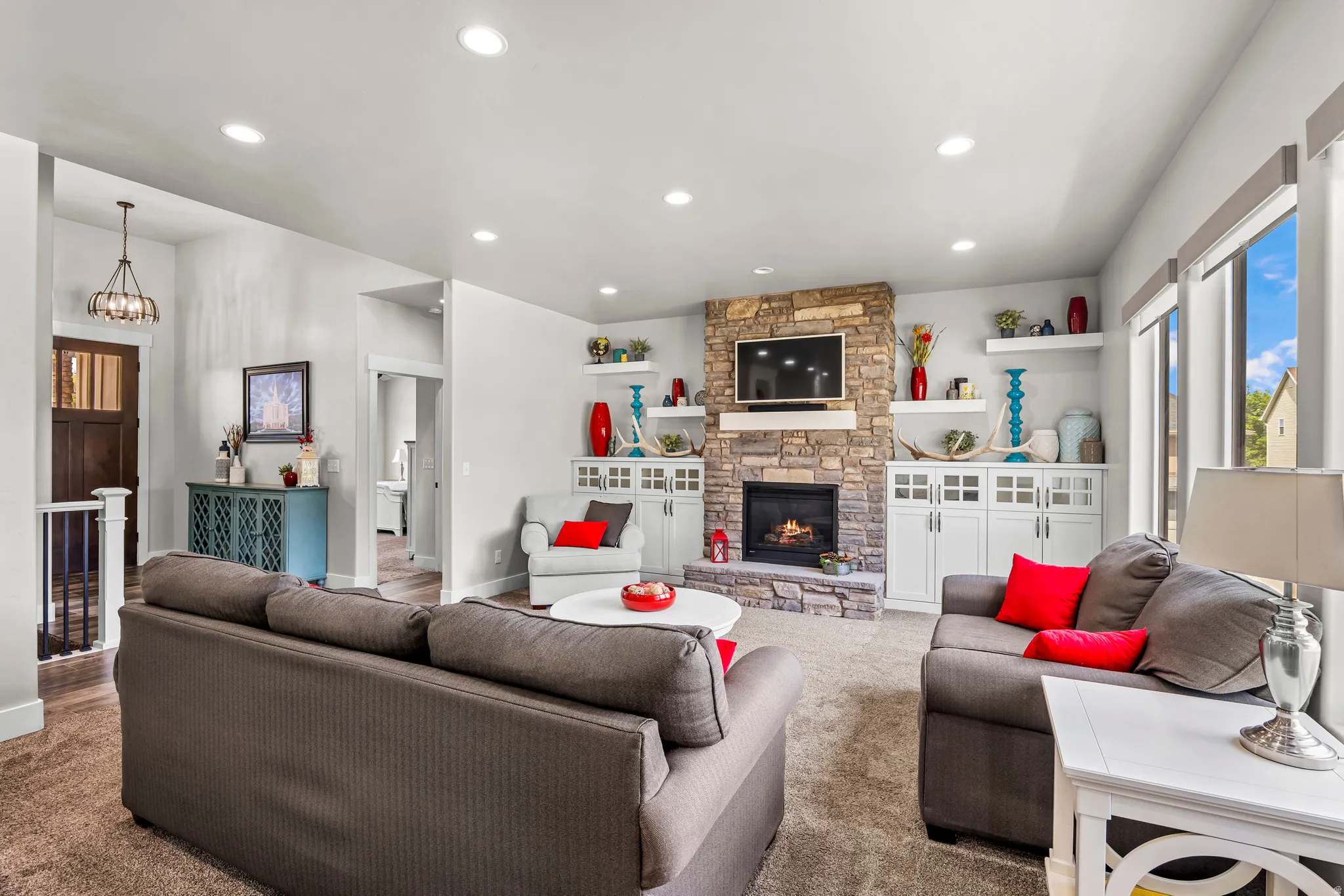Living room featuring a stacked stone fireplace with a white mantel, recessed lighting, and built-in white cabinetry with display shelving