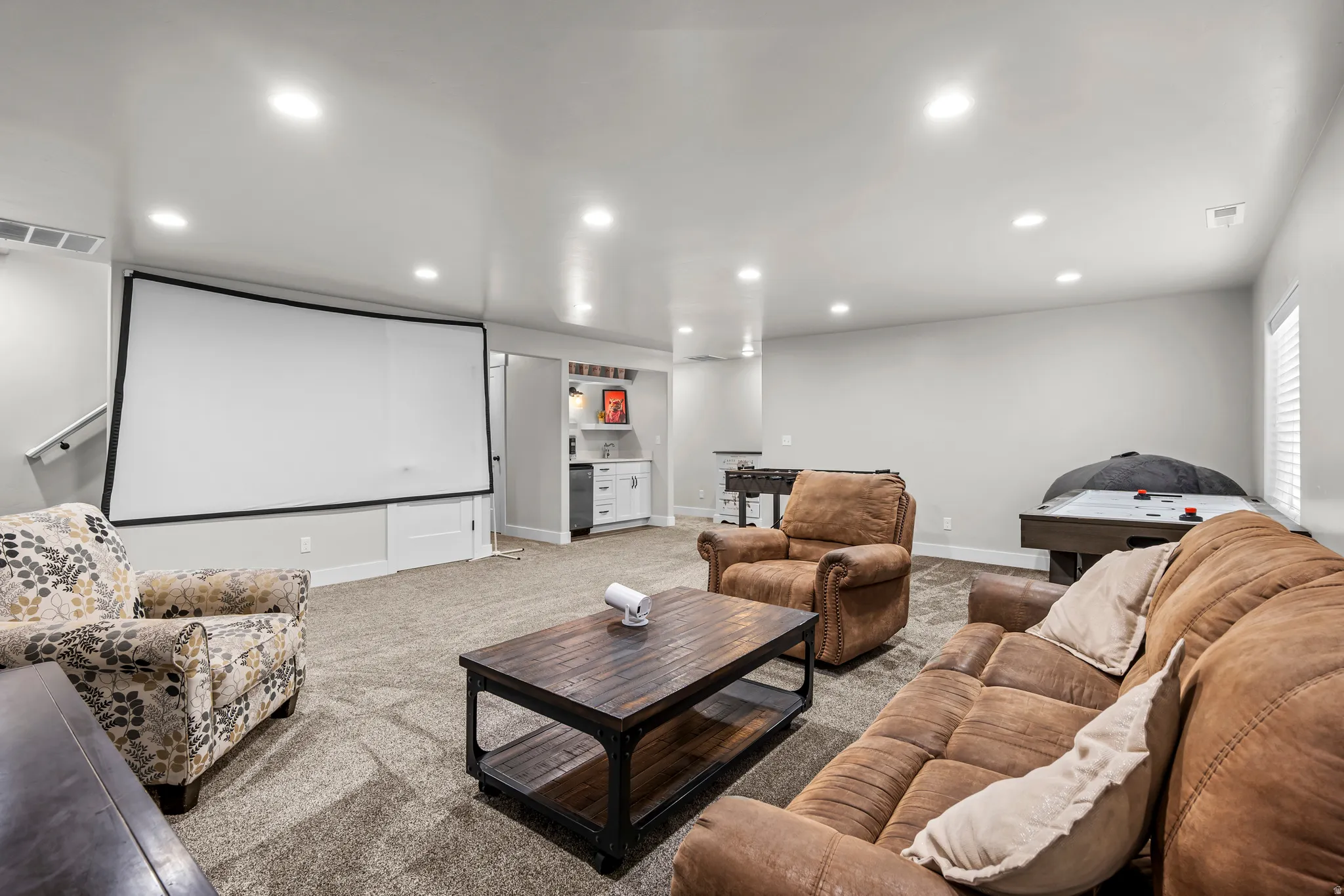 Spacious entertainment room featuring a large projection screen, recessed lighting, and a built-in wet bar with white cabinetry