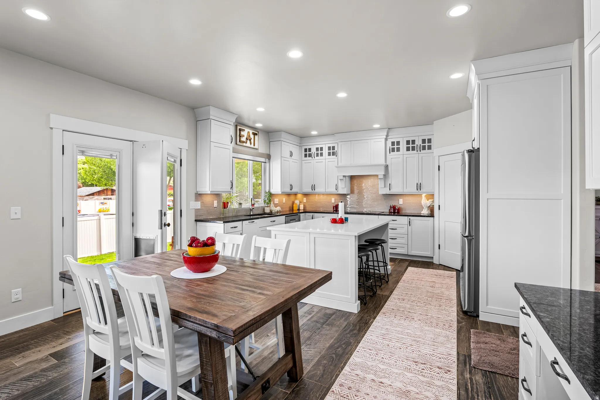 Spacious kitchen featuring white cabinetry, dark countertops, a large island with seating, stainless steel appliances, and wood-finish flooring