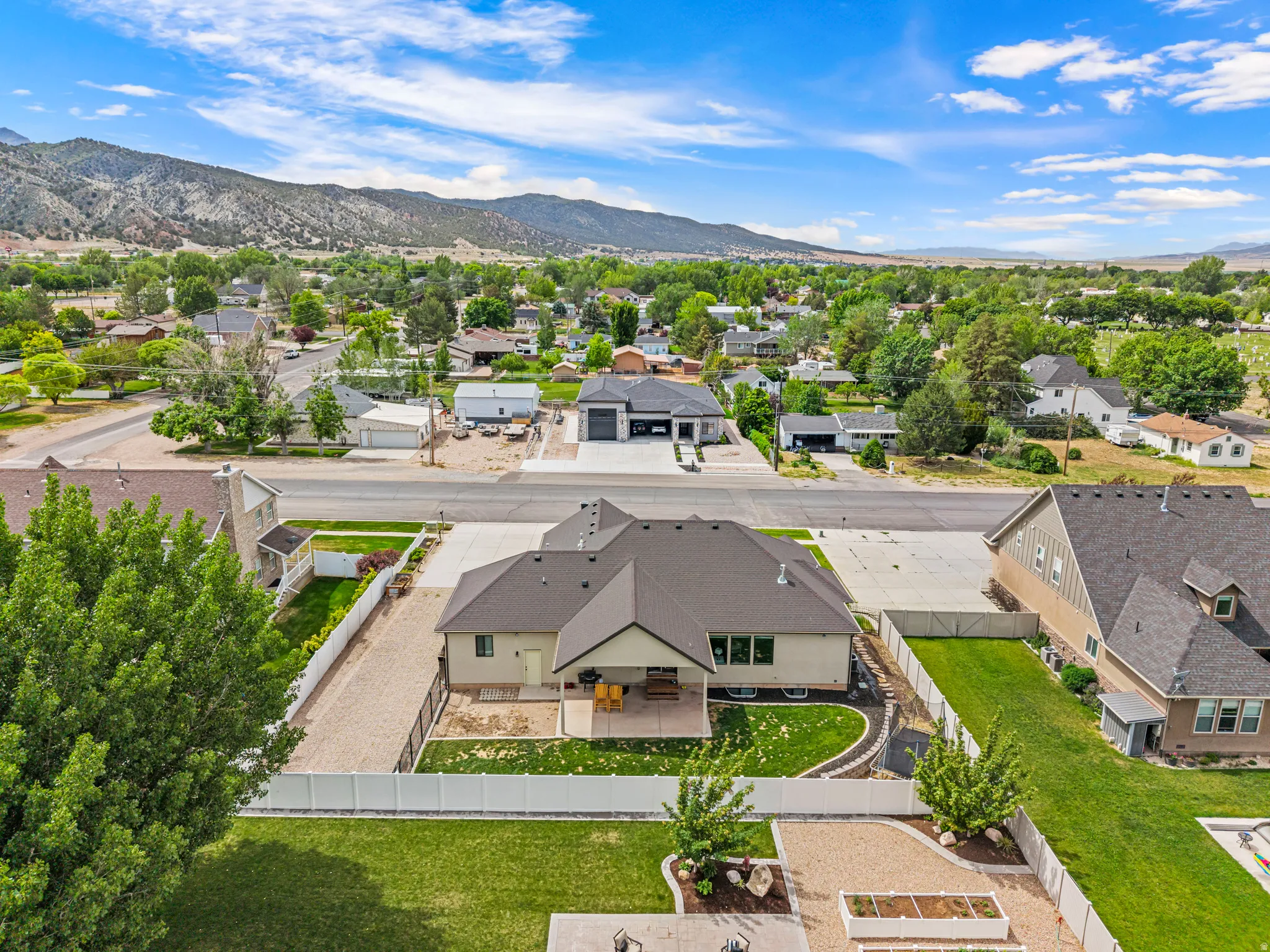 Aerial perspective showcasing a single-story residence with a dark shingle roof, a manicured backyard with a green lawn, and a white fence enclosing the property