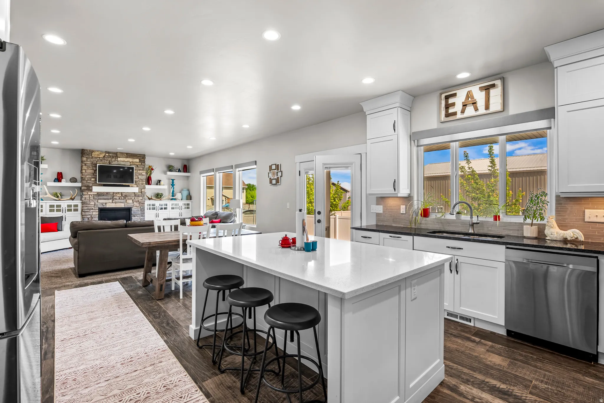 Contemporary kitchen featuring a large center island with seating, white shaker cabinetry, dark countertops, and stainless steel appliances