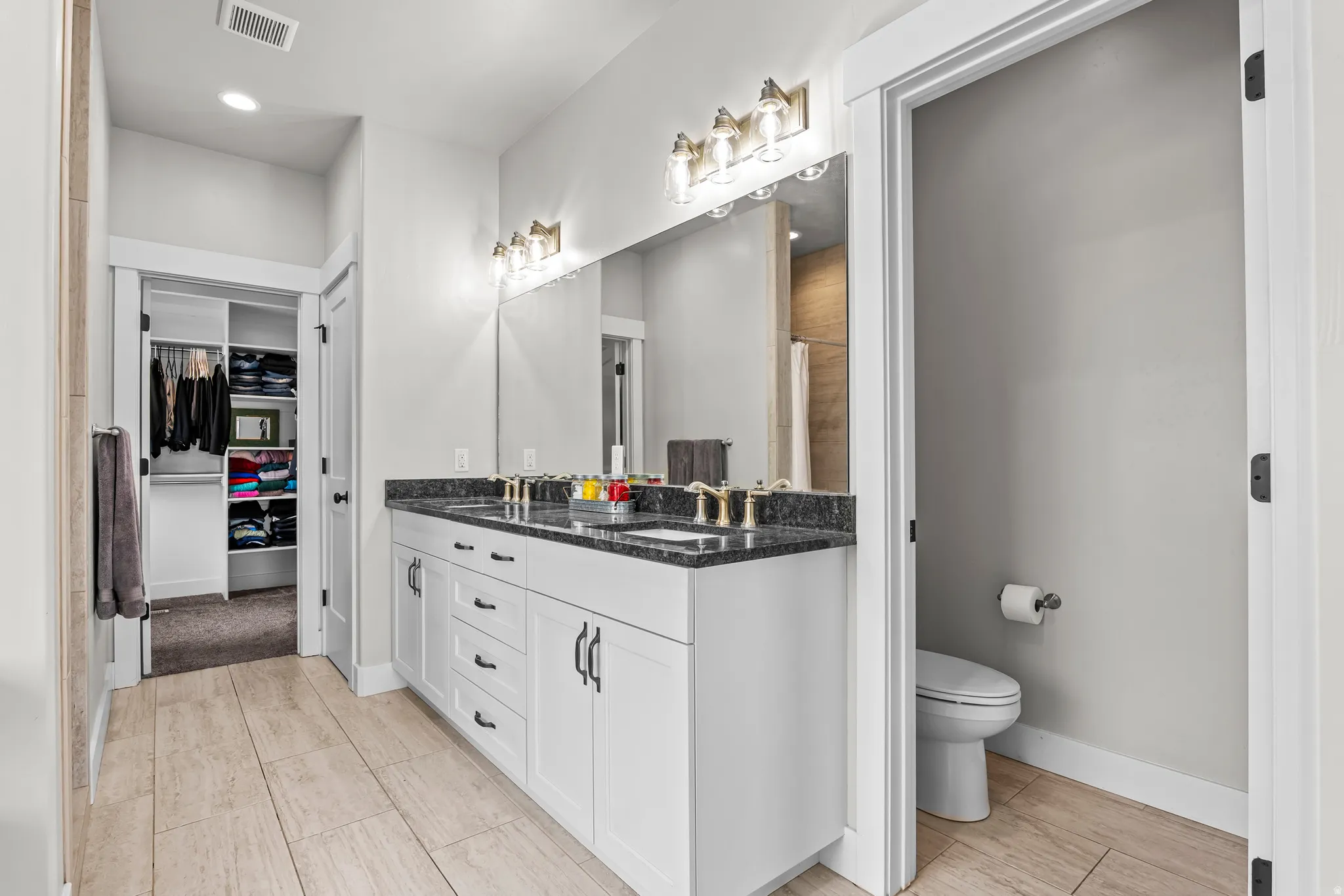 Bathroom featuring a dual vanity with white cabinetry, dark stone countertops, and gold-finish fixtures