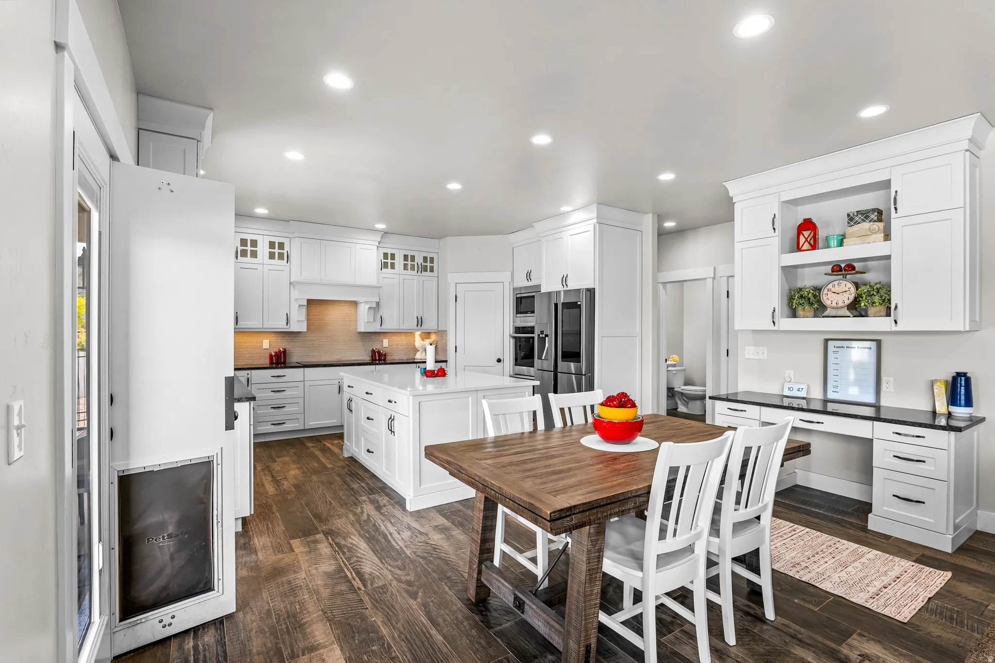 Open-concept kitchen featuring white shaker cabinetry, an expansive central island with a quartz countertop, stainless steel appliances, recessed lighting, and wood-finish flooring