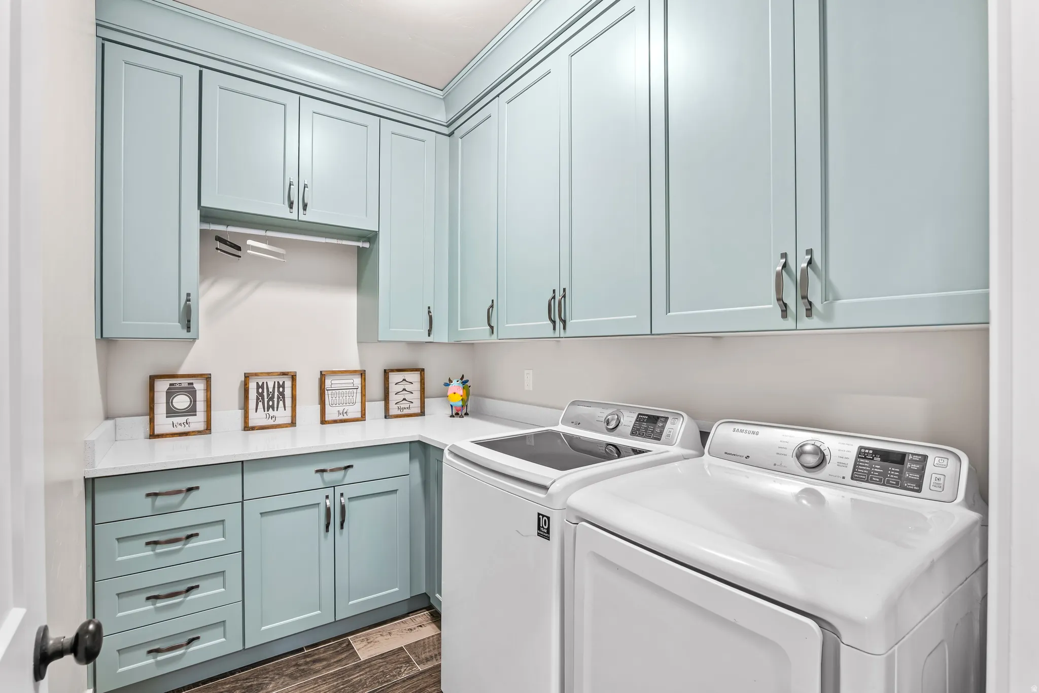 Laundry room featuring extensive light blue cabinetry with dark hardware, white countertops, and wood-finish flooring