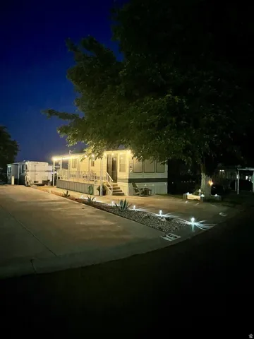 Manufactured home featuring a raised porch, full outdoor lighting, mature tree, and a rock-filled landscape bed with agave plants