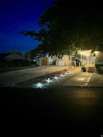 Concrete driveway with integrated ground lighting leading to a covered porch with string lights