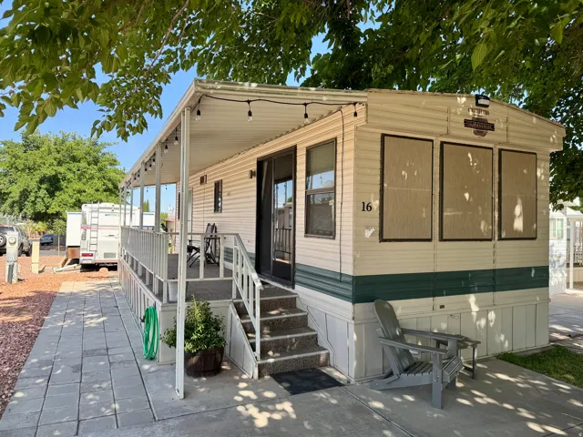 Exterior featuring an elongated covered front porch, white horizontal siding with a dark green accent, a paver stone walkway, and a partial view of mature trees