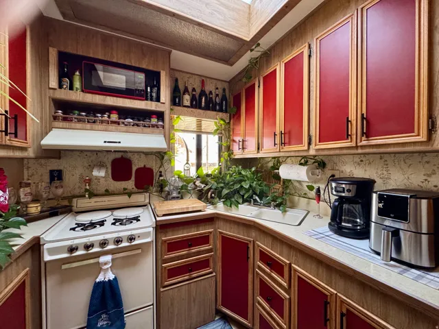 Kitchen featuring wood-finish cabinetry with red paneled inserts, a built-in microwave, an integrated range hood, a white four-burner electric range, and a white sink