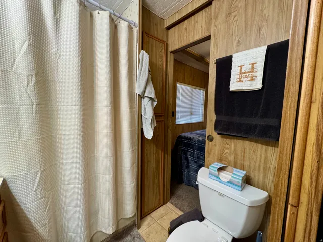 Bathroom with wood-finish paneling, a white toilet, and a shower area featuring a light-colored shower curtain