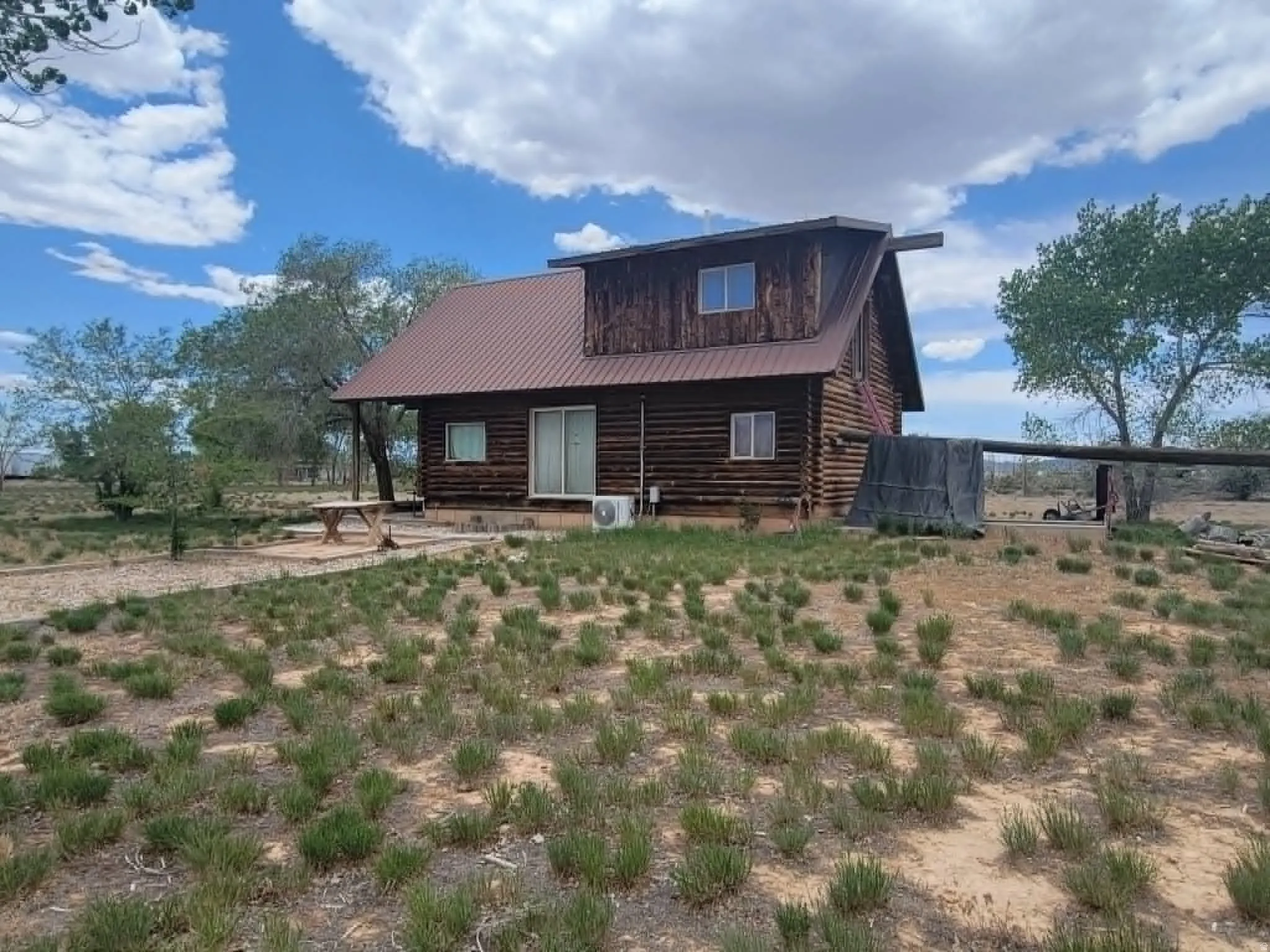 Log cabin exterior featuring a metal roof, dormer windows, sliding glass door, and a gravel patio area