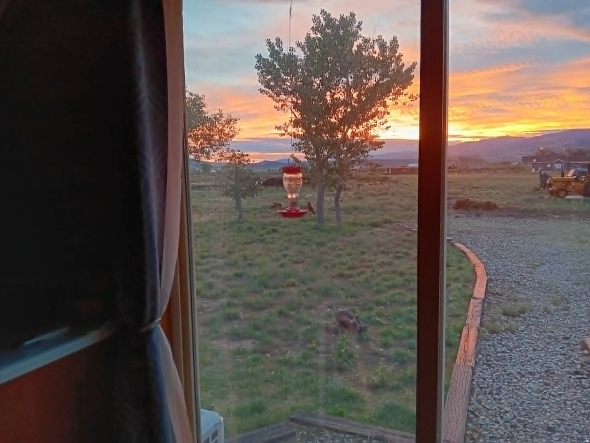 Expansive outdoor scenery with a vibrant sunset backdrop, featuring mature trees and a gravel pathway