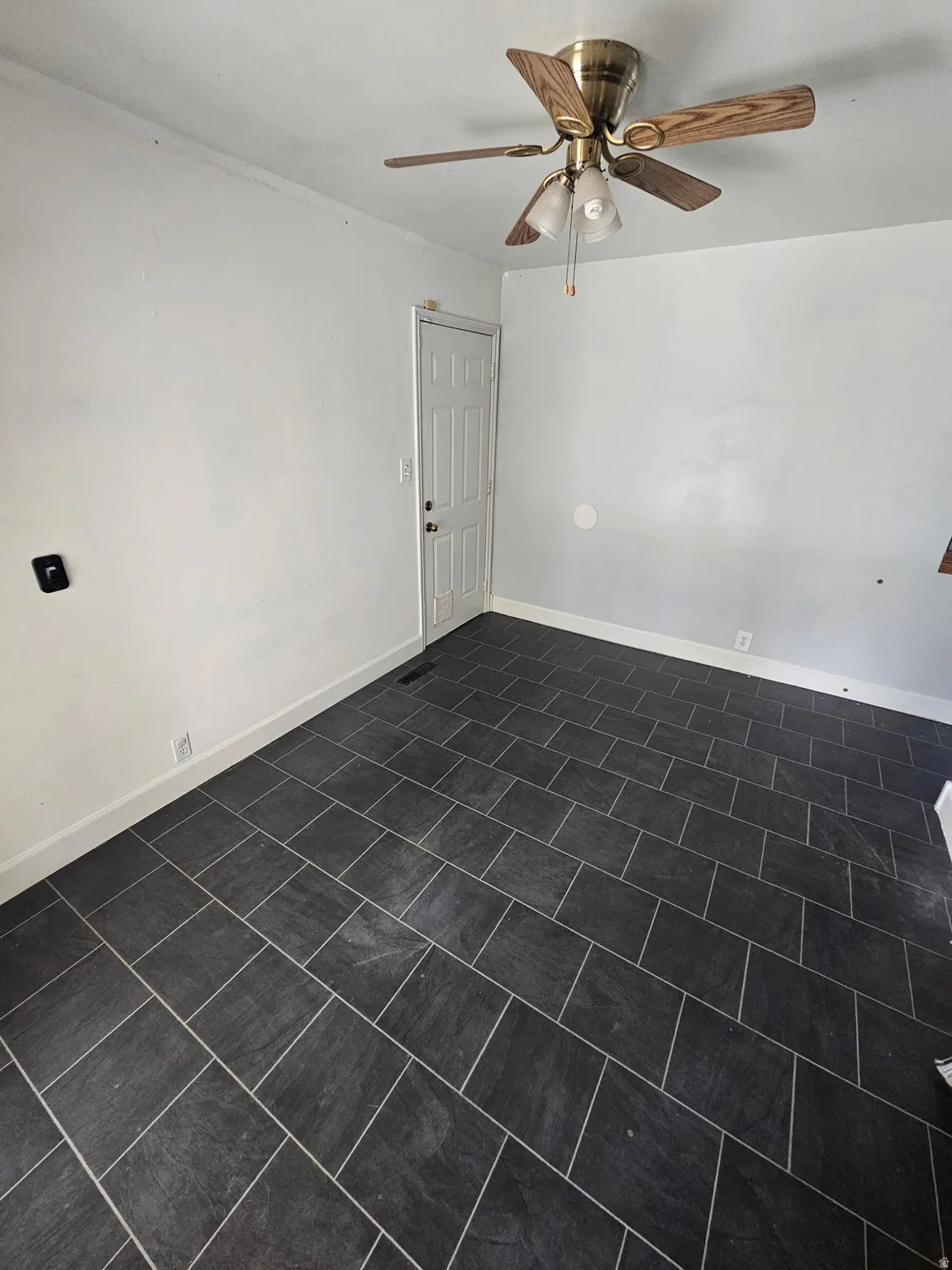 Spacious room featuring dark rectangular tile flooring, white baseboards, and a ceiling fan with light kit