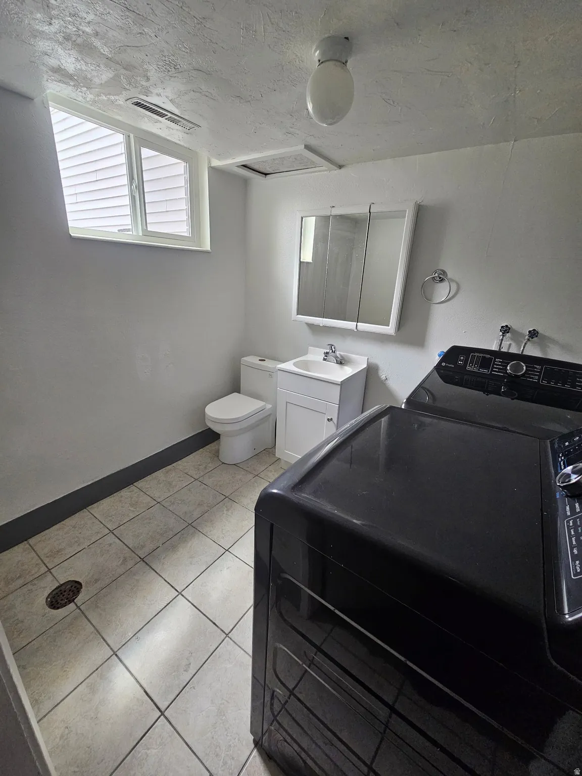Utility room featuring tile flooring, a window, flush mount ceiling light, and a vanity with a mirrored medicine cabinet