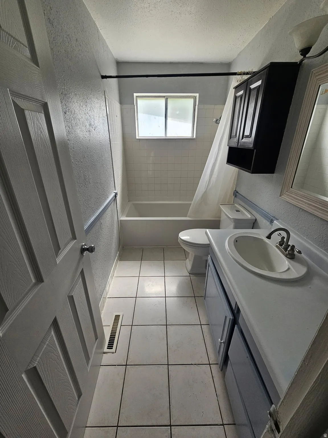 Bathroom featuring a white tile floor, a built-in bathtub with white tile surround, a window, a single vanity with an integrated sink, and a wall-mounted cabinet