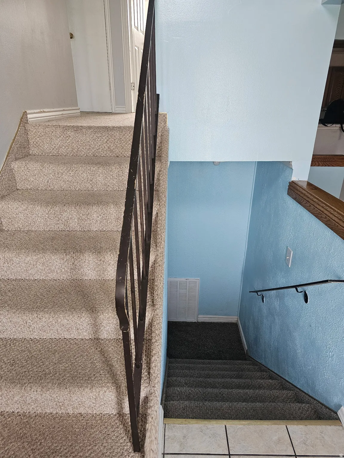 Carpeted staircase featuring a wrought iron handrail and light blue wall tones