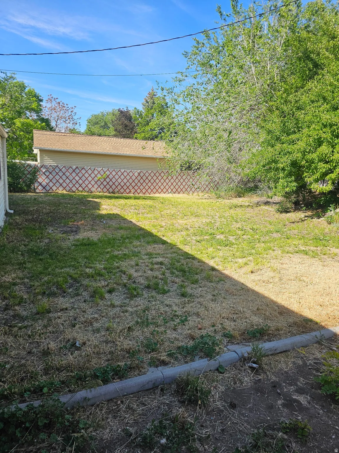 Expansive backyard featuring a partial lattice fence and a detached building with beige siding and a shingle roof