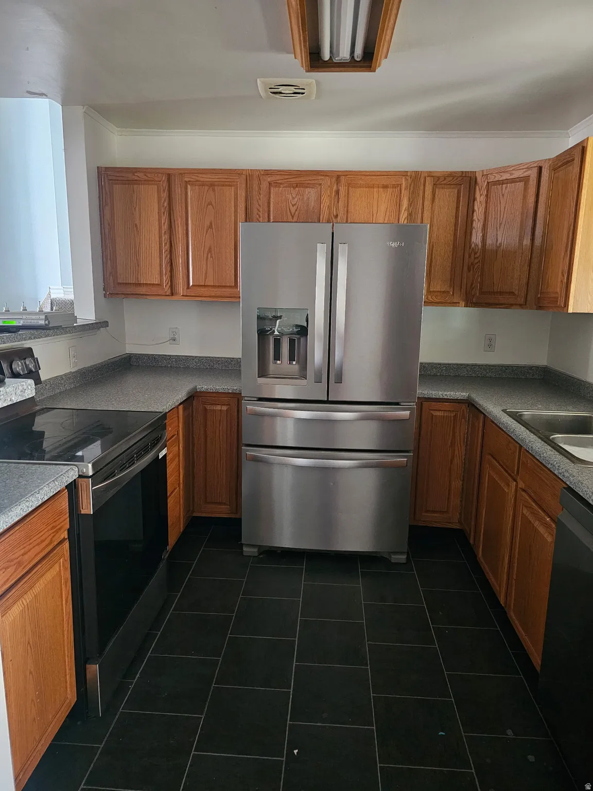 U-shaped kitchen featuring wood cabinetry, dark speckled countertops, and black square tile flooring