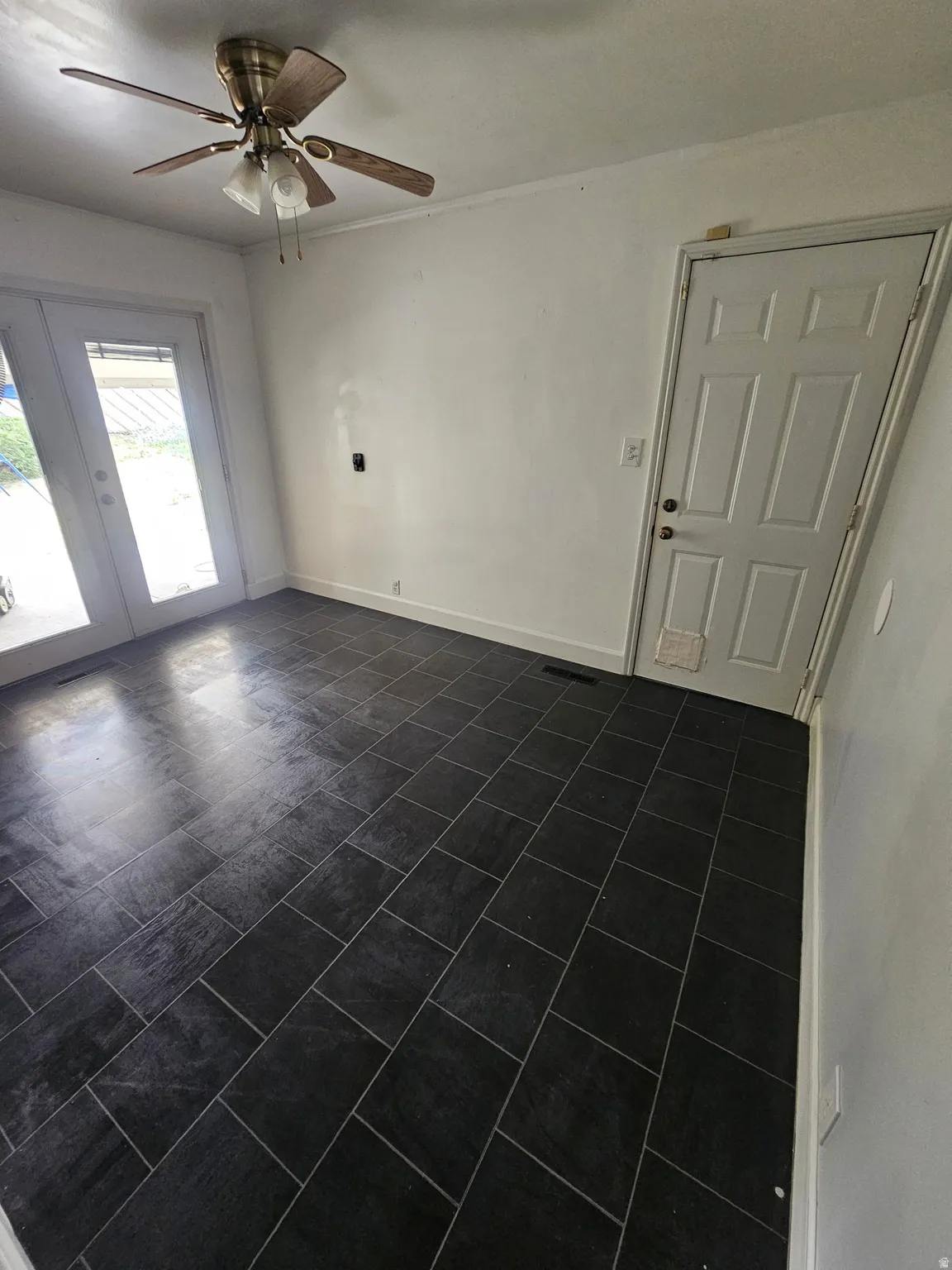 Room featuring dark rectangular tile flooring, a white paneled door, and a ceiling fan with integrated lighting