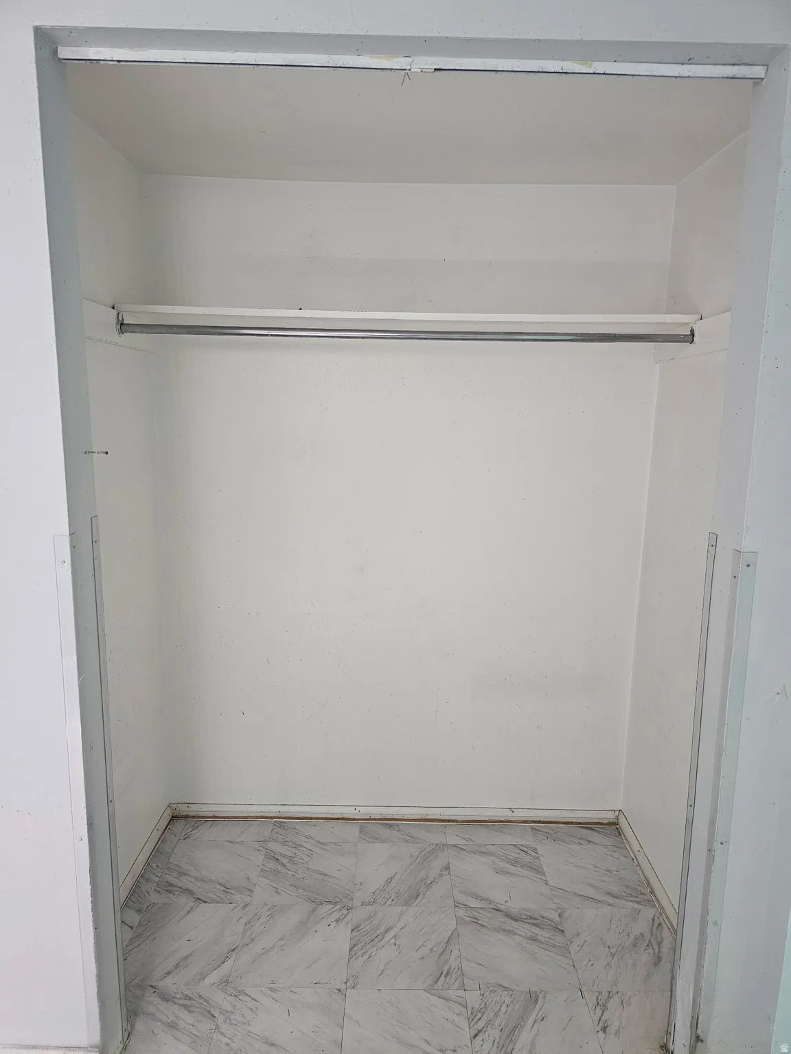 Spacious closet featuring a single hanging rod, white painted walls, and patterned tile flooring
