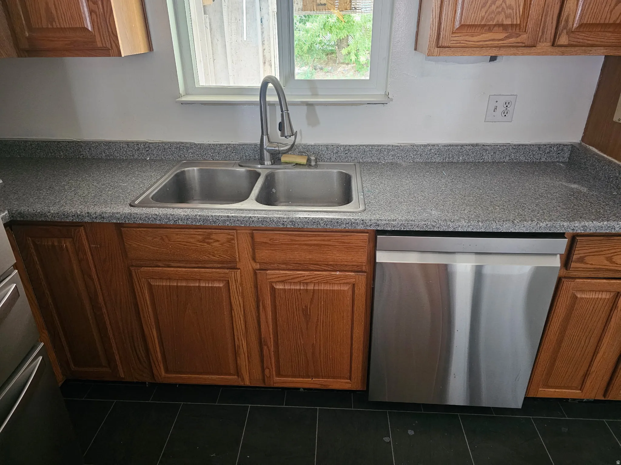 Kitchen workstation featuring a double basin stainless steel sink with a gooseneck faucet, laminate countertops, wood cabinetry, and a stainless steel dishwasher