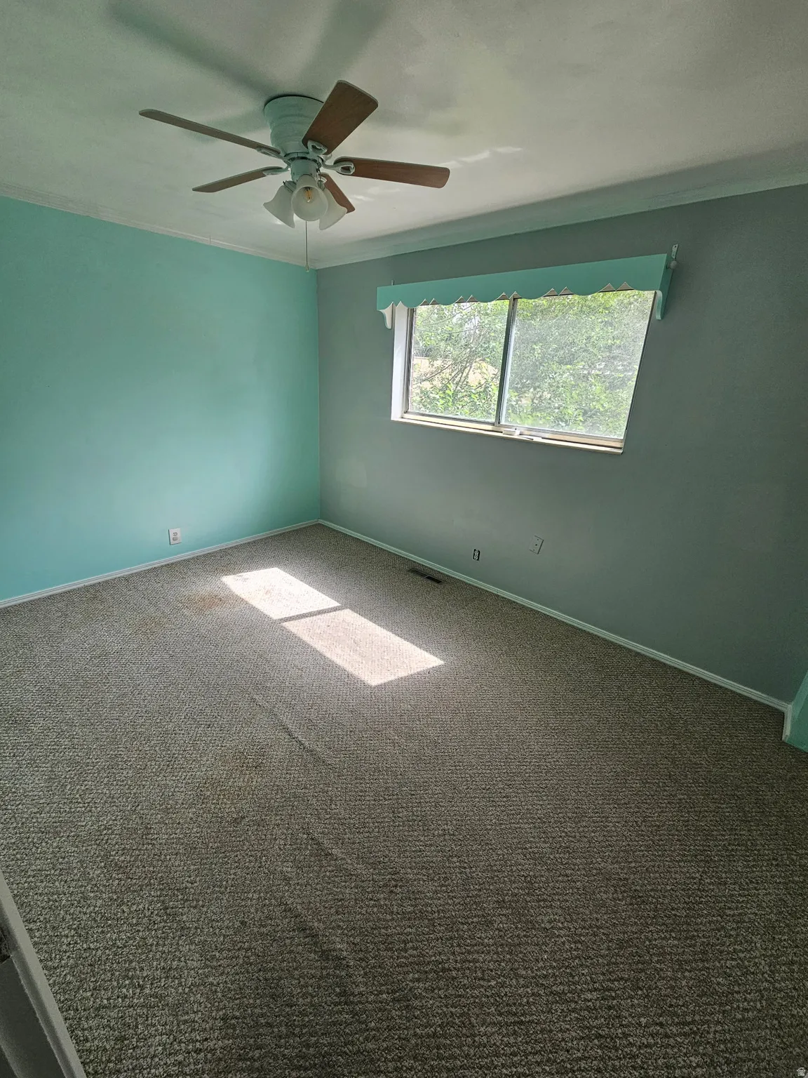 Room with two-tone wall paint, a ceiling fan with light fixture, and a window featuring an exterior view