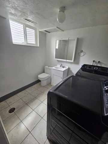 Utility room featuring tile flooring, a window, flush mount ceiling light, and a vanity with a mirrored medicine cabinet