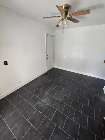 Spacious room featuring dark rectangular tile flooring, white baseboards, and a ceiling fan with light kit