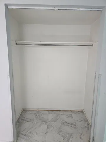 Spacious closet featuring a single hanging rod, white painted walls, and patterned tile flooring