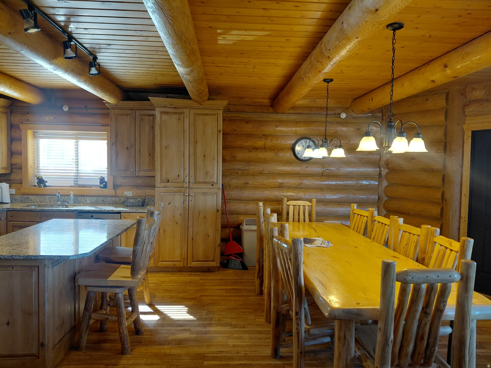 Expansive kitchen and dining area featuring natural wood log walls, a wood-finish ceiling with exposed log beams, and wood-finish flooring