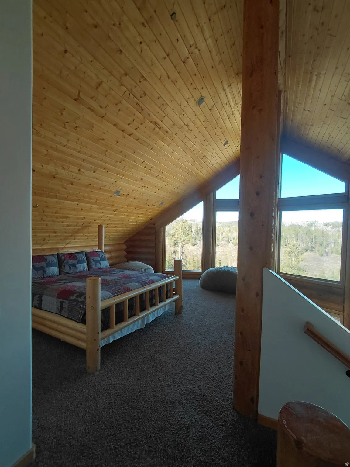 Loft space featuring extensive wood-paneled walls and ceiling, exposed structural log beams, and broad windows offering expansive outdoor views