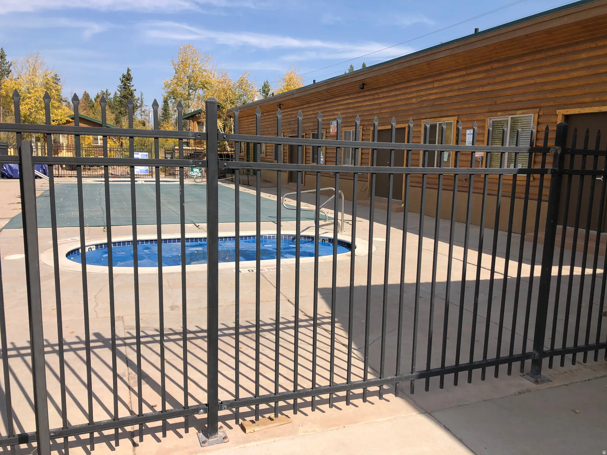 Fenced outdoor pool area featuring a covered main pool and an uncovered smaller pool