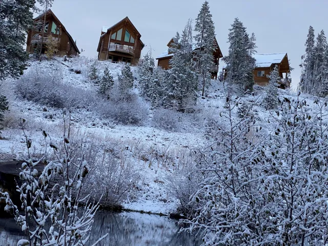 Cabin-style property featuring a pitched roofline, natural wood siding, and prominent windows, surrounded by snow-covered evergreen trees