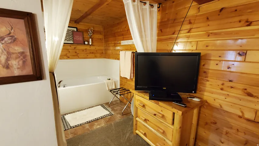 Wood-paneled interior featuring a built-in soaking tub with surround, a wood-finish dresser, and a wall-mounted shelving unit