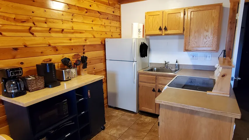 Compact kitchen featuring a ceramic tile floor, wood panel accent wall, oak cabinetry, a stainless steel sink, and a built-in electric cooktop