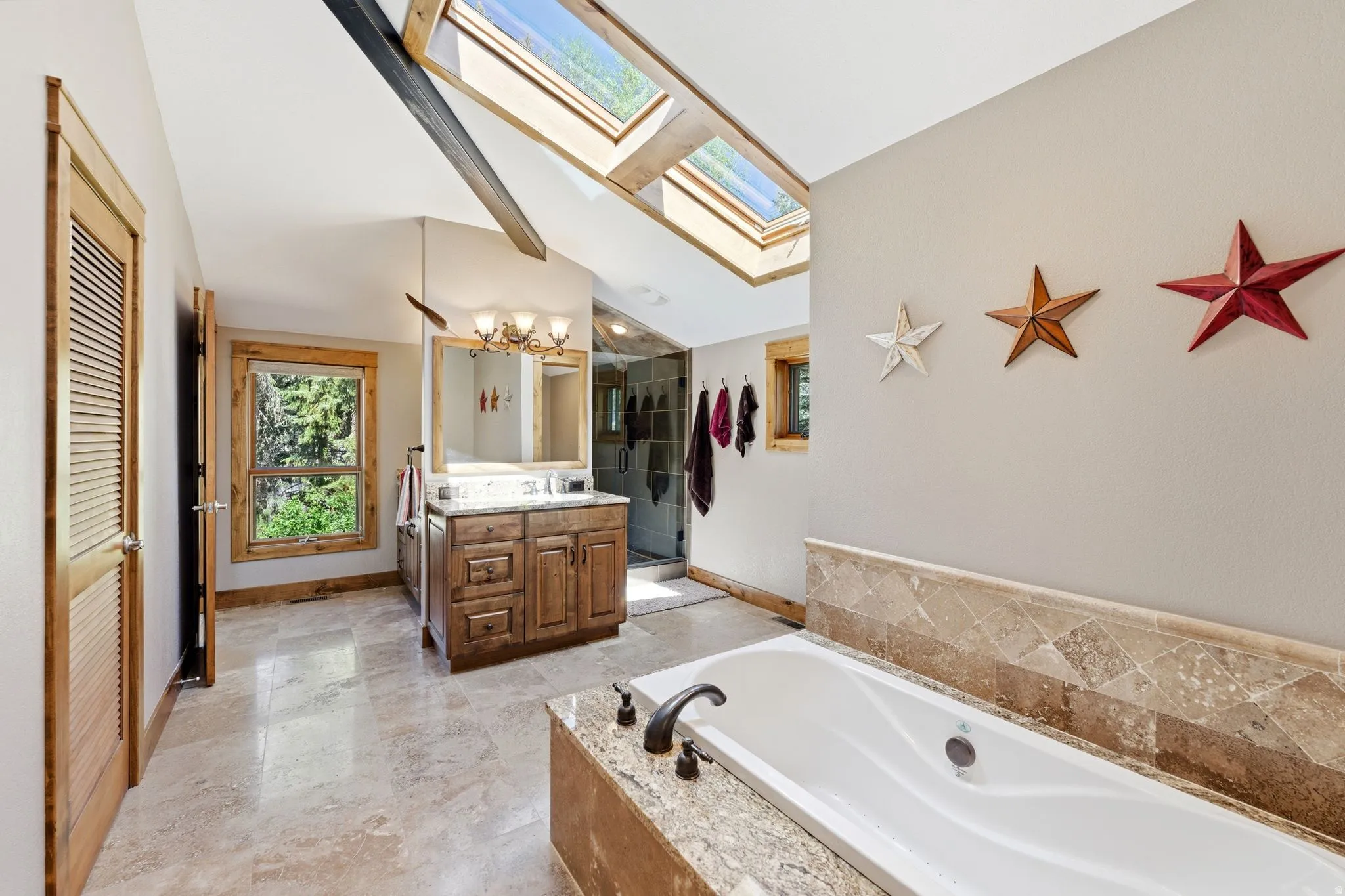 Bathroom featuring dual skylights, a built-in soaking tub with stone surround, a wood vanity with a granite countertop, and tile flooring