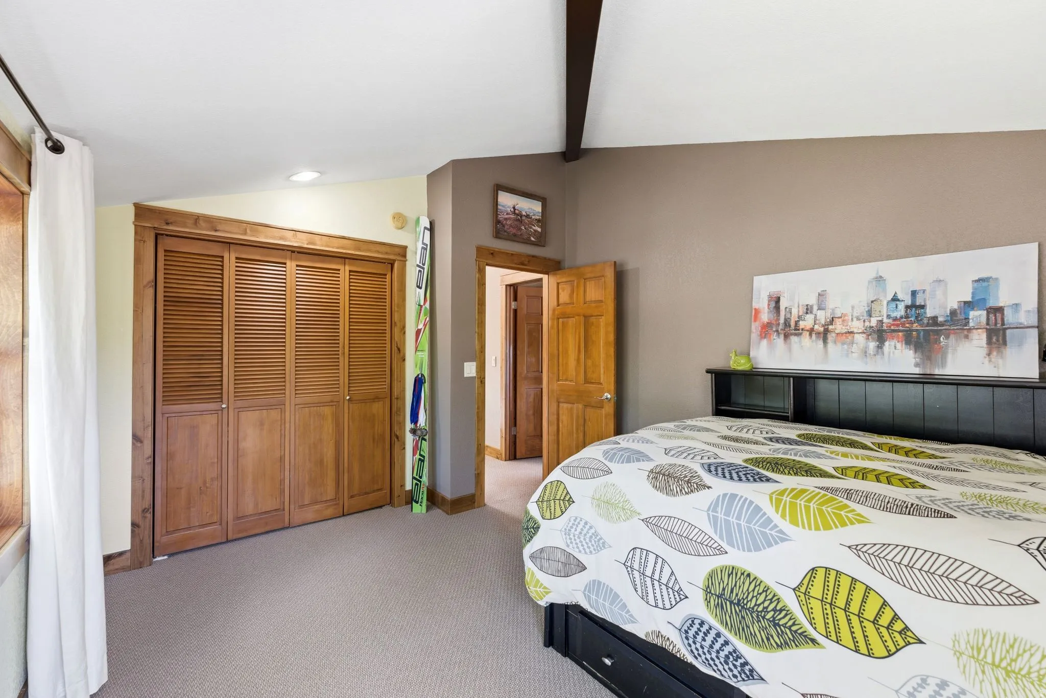 Bedroom featuring a bi-fold louvered closet, neutral carpet flooring, and a vaulted ceiling with exposed beams