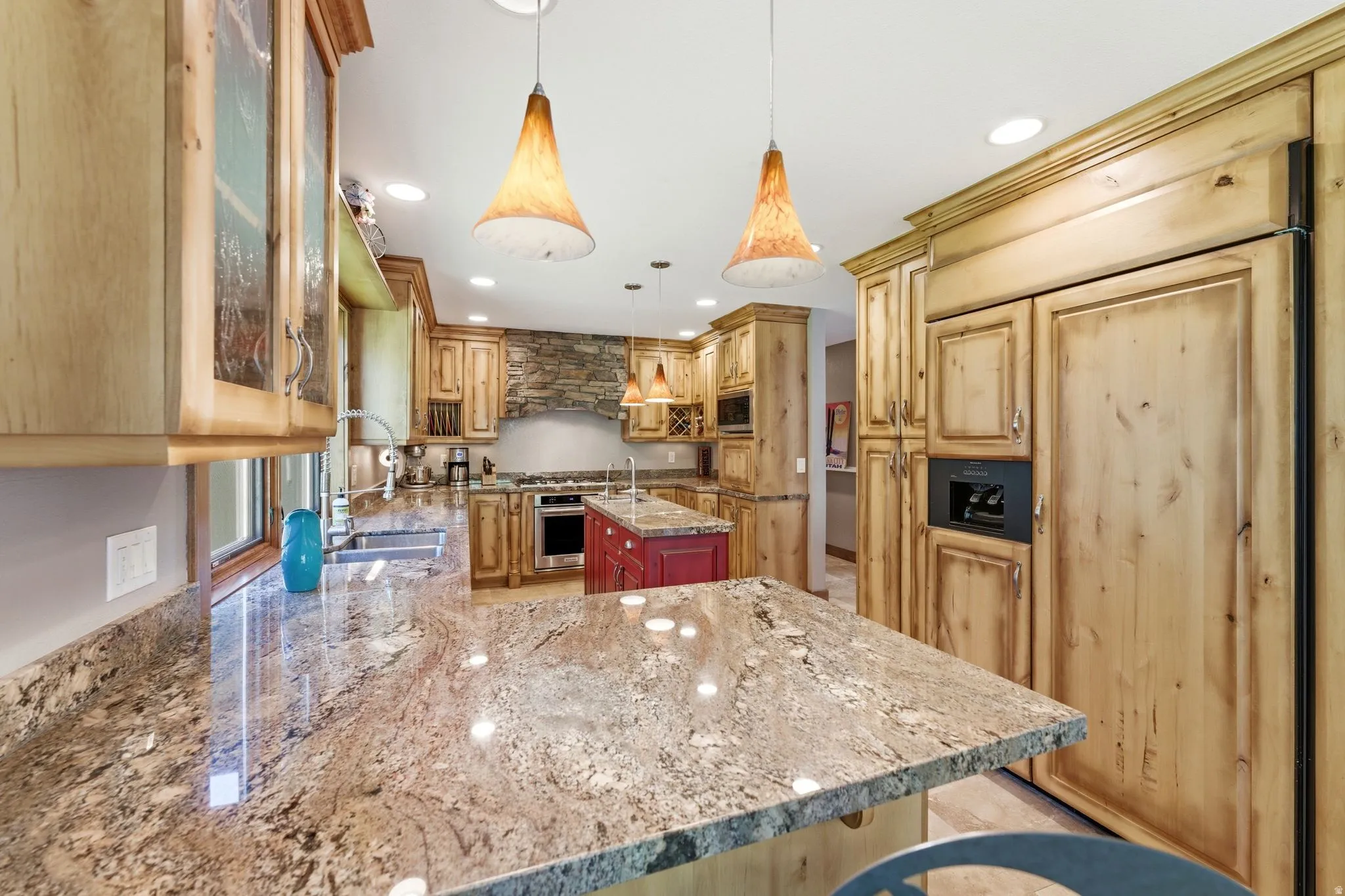 Kitchen featuring wood cabinetry, stone countertops, a central island with contrasting red cabinetry, stainless steel appliances, and recessed lighting